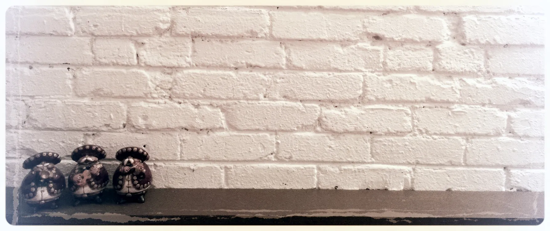 Three small figurines on a shelf against a white brick wall at the studio